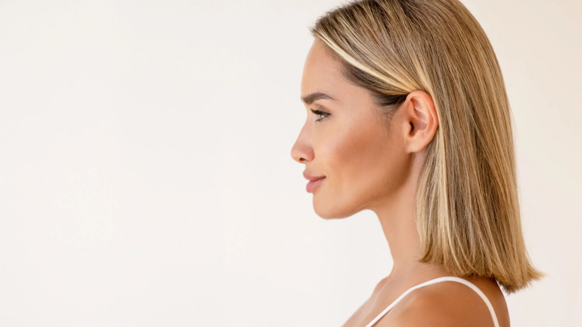 Woman with a blonde bob in profile against a soft cream background