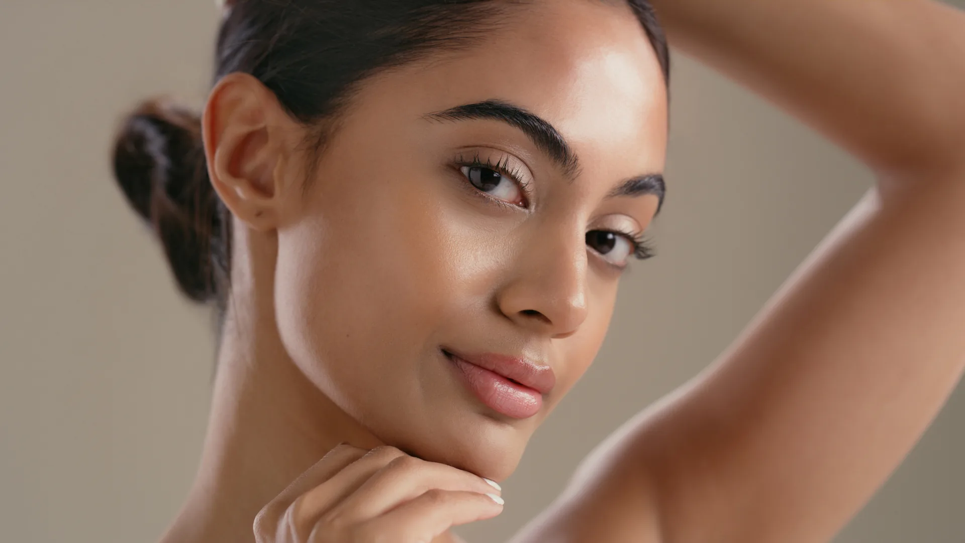 Woman with her hair in a bun resting her chin on her hand, arm raised behind her head
