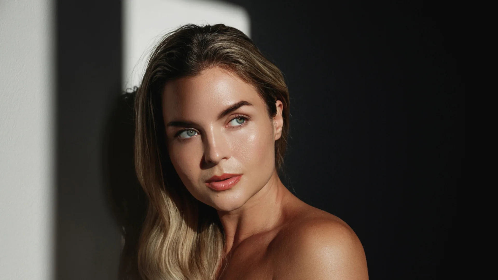 Woman with long hair and glowing skin looking up in dramatic window light