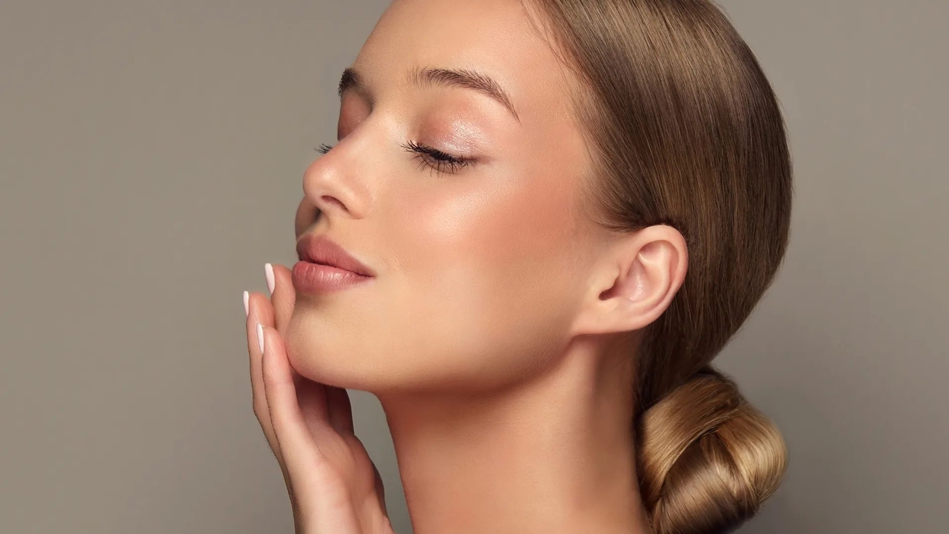 Woman in profile with eyes closed and a low bun, fingertips resting on her chin