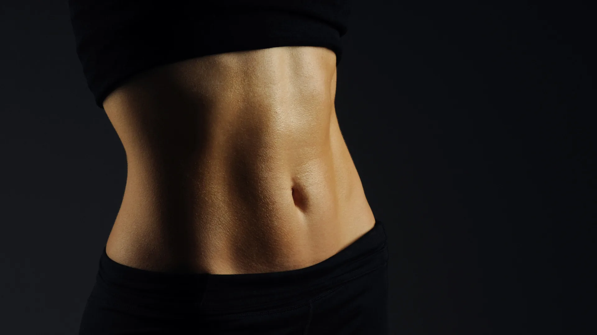 Close-up of a woman's toned midsection against a black background