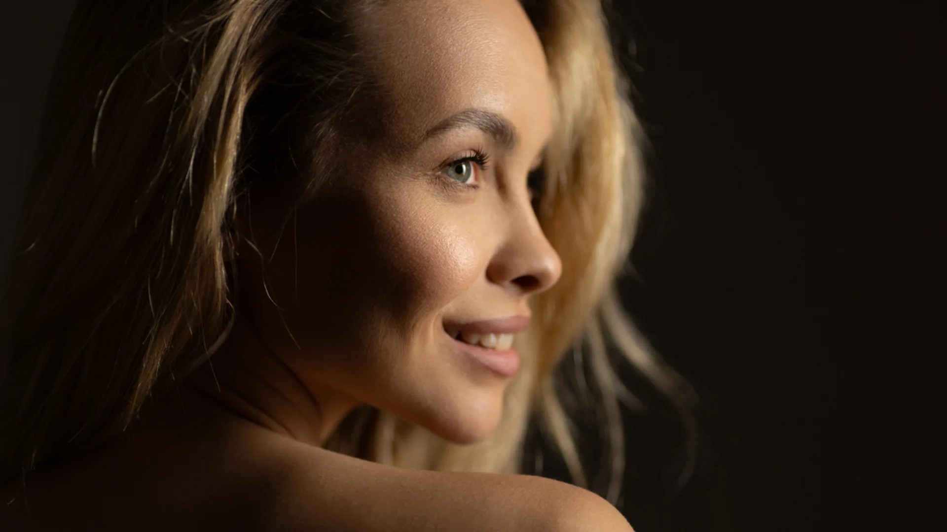 Smiling woman with blonde hair in profile against a dark background