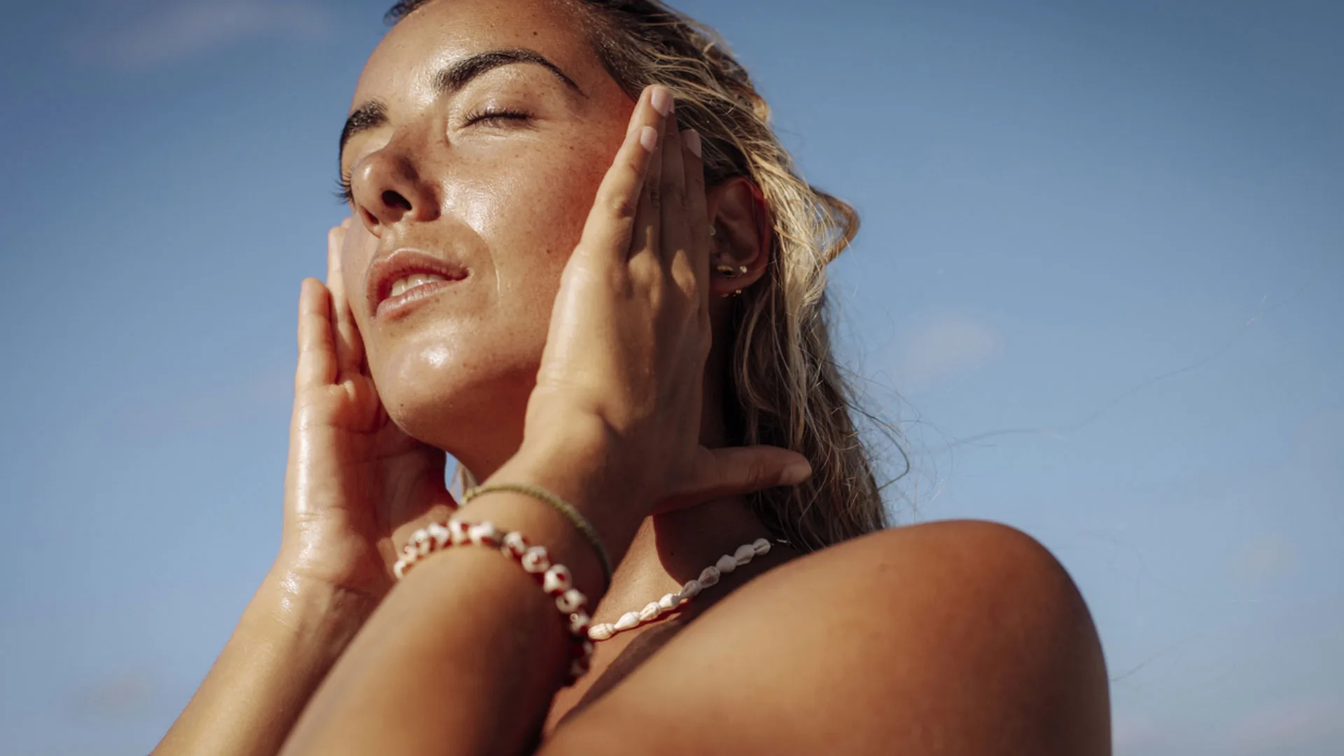 Woman with freckles and eyes closed, face lifted to the sun against a blue sky