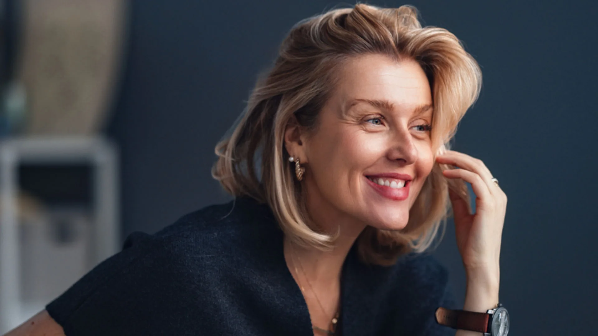 Laughing woman with blonde hair touching her face, looking to the side