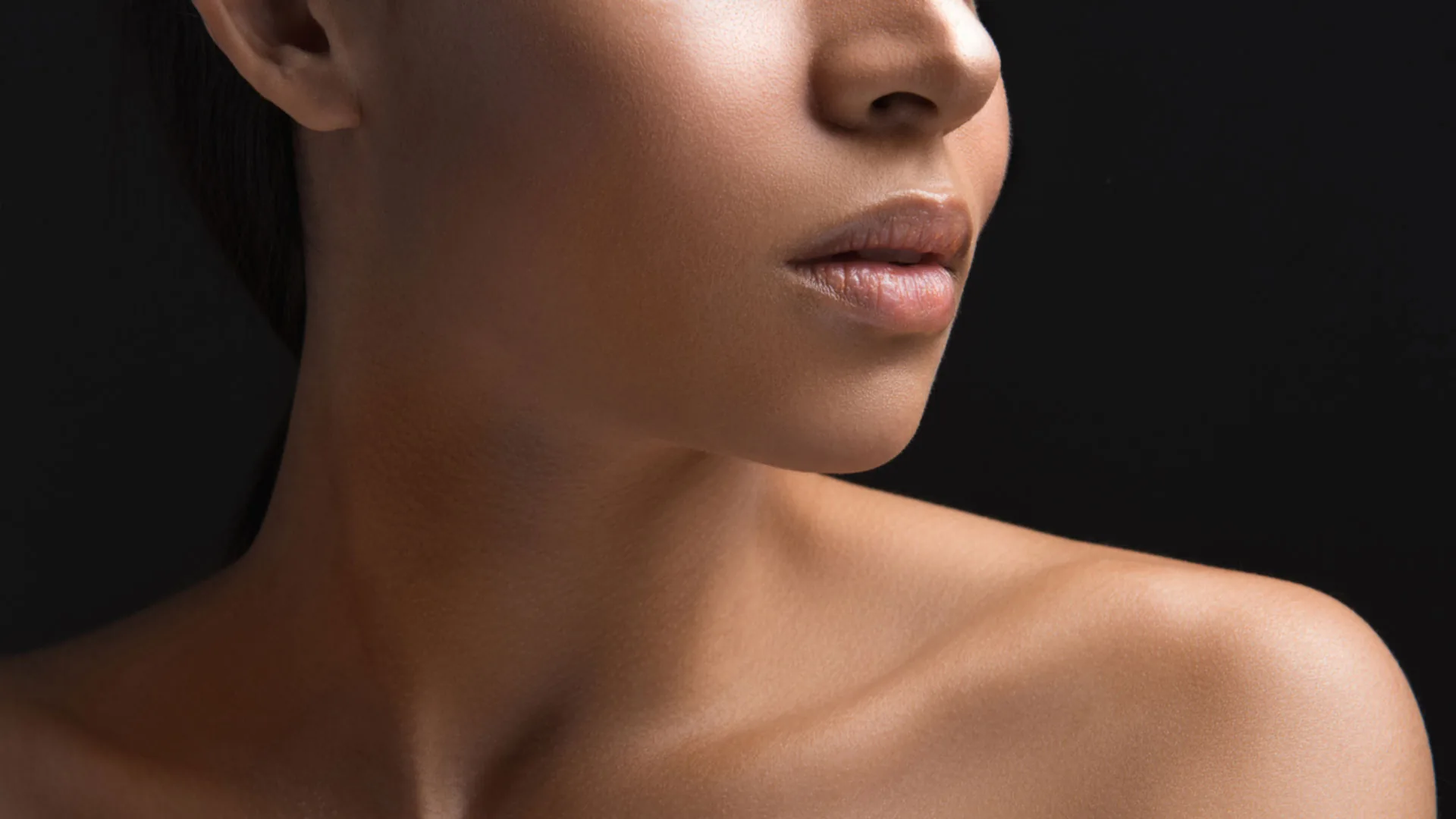 Close-up of a woman's lips, jawline, and shoulder against a black background