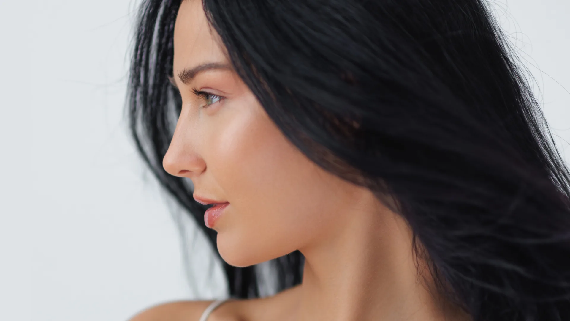 Woman with long black hair in profile against a light background