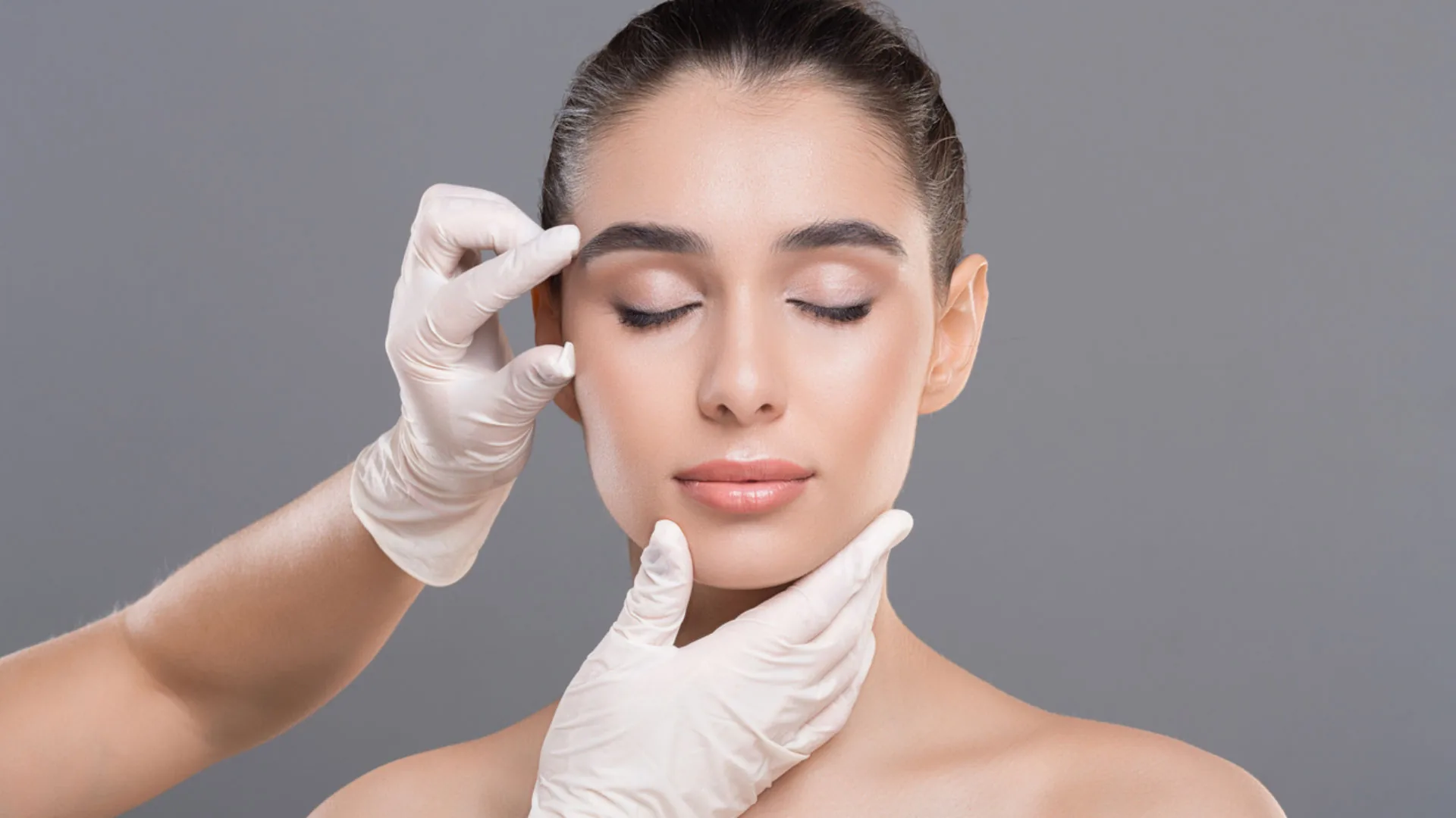 Gloved hands gently examining a woman's face as she sits with eyes closed