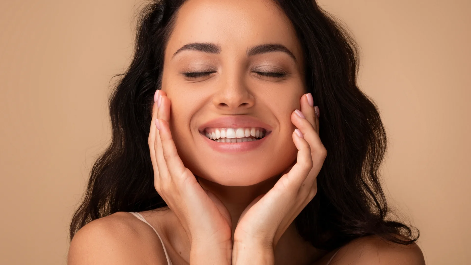 Smiling woman with eyes closed cradling her cheeks in her hands