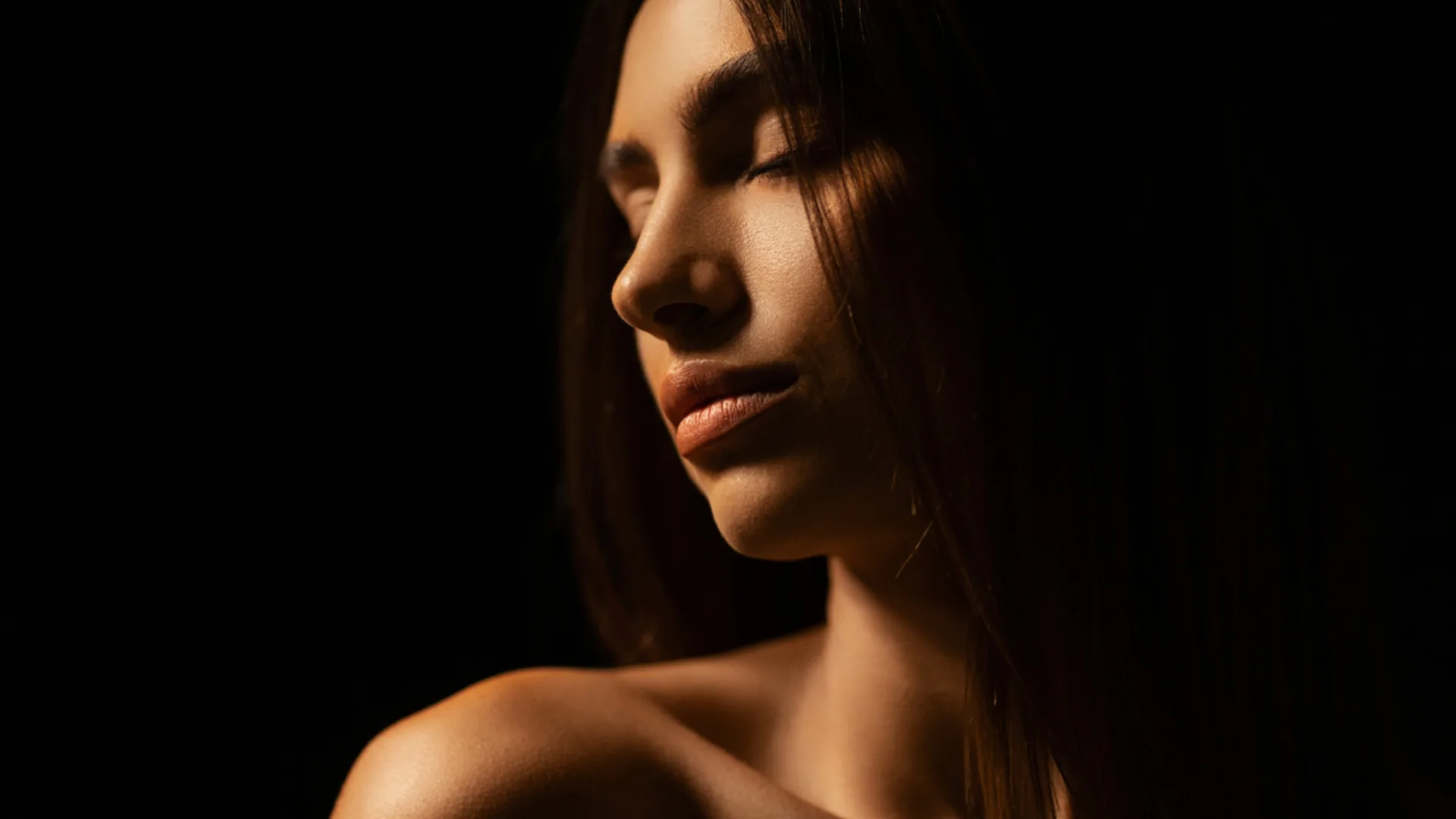 Woman with long dark hair and eyes closed in dramatic low light