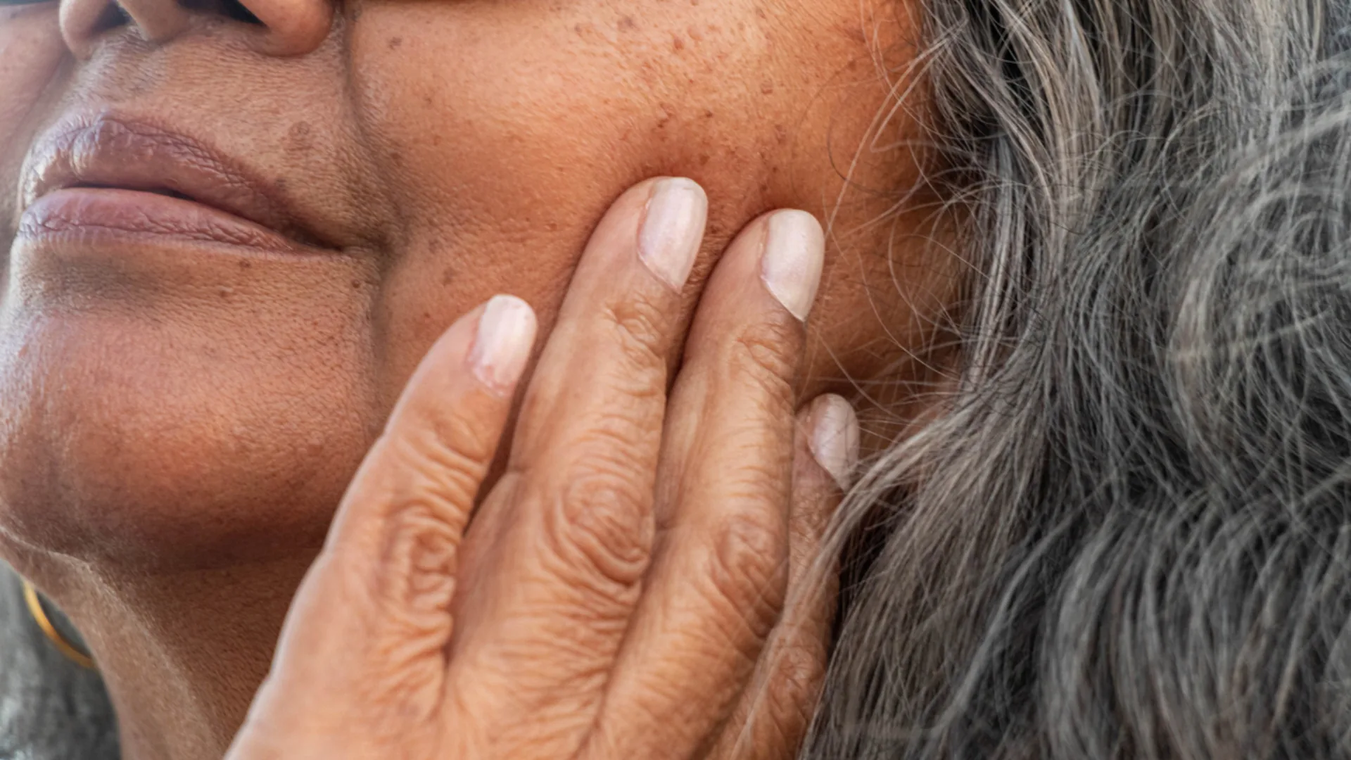 Close-up of a mature woman touching her cheek, showing skin texture and sunspots