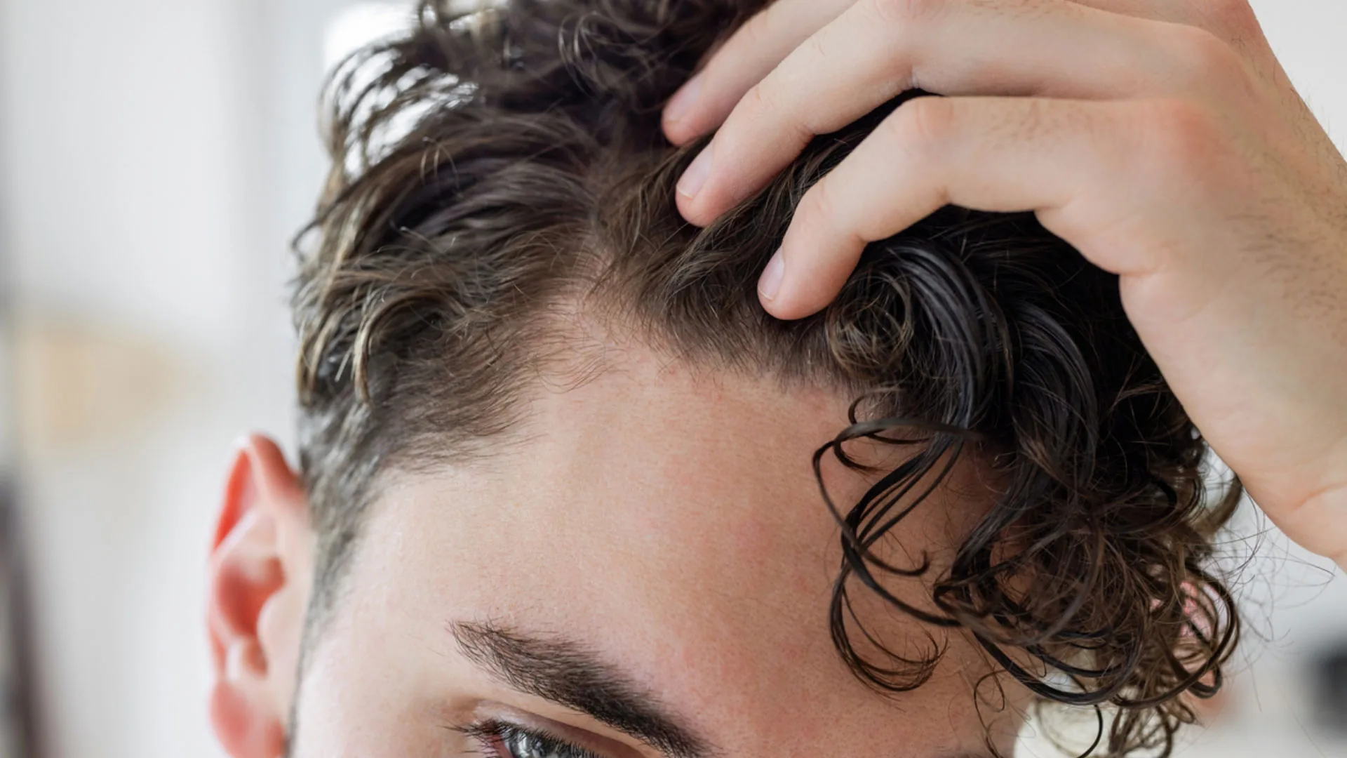 Man running his fingers through his curly hair near the hairline