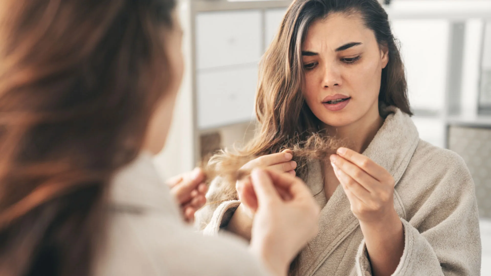 Woman looking concerned while inspecting the ends of her hair in a mirror