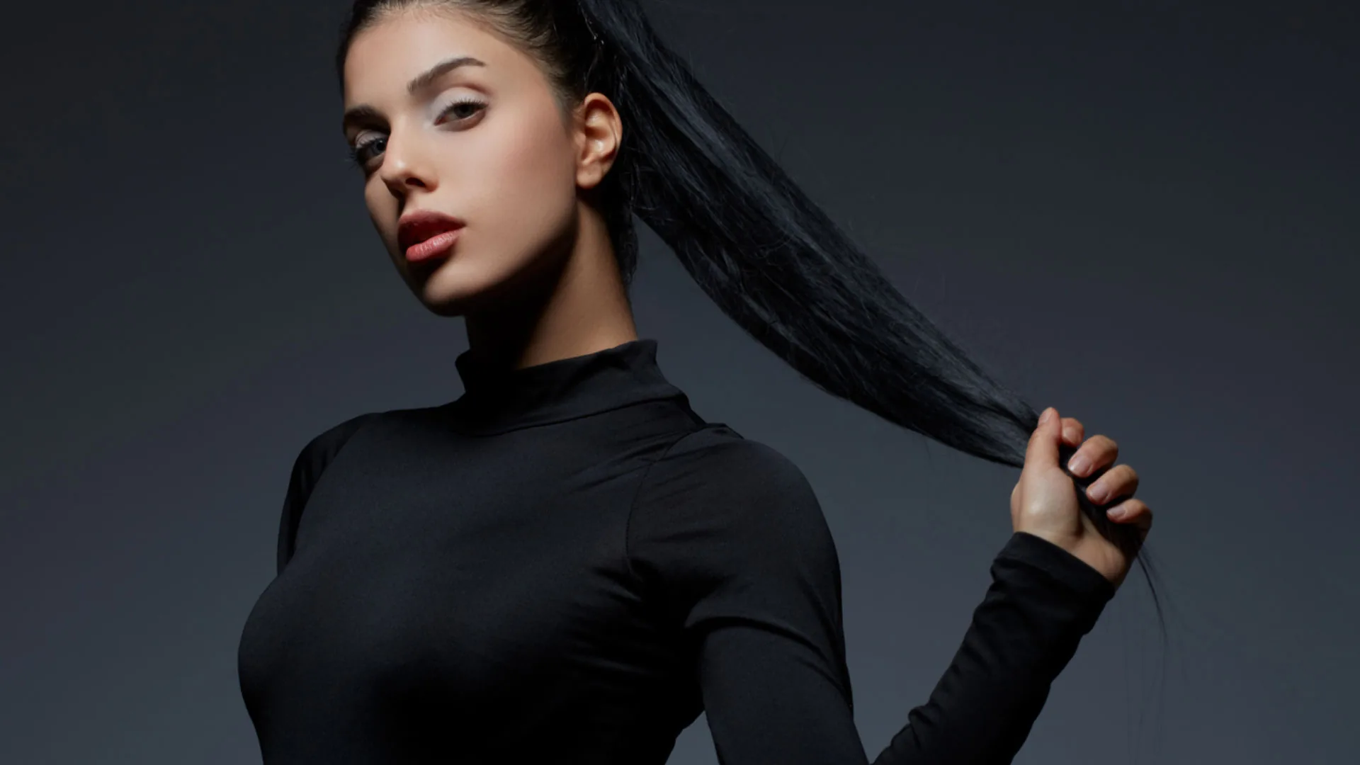 Woman in a black turtleneck holding her long, dark ponytail