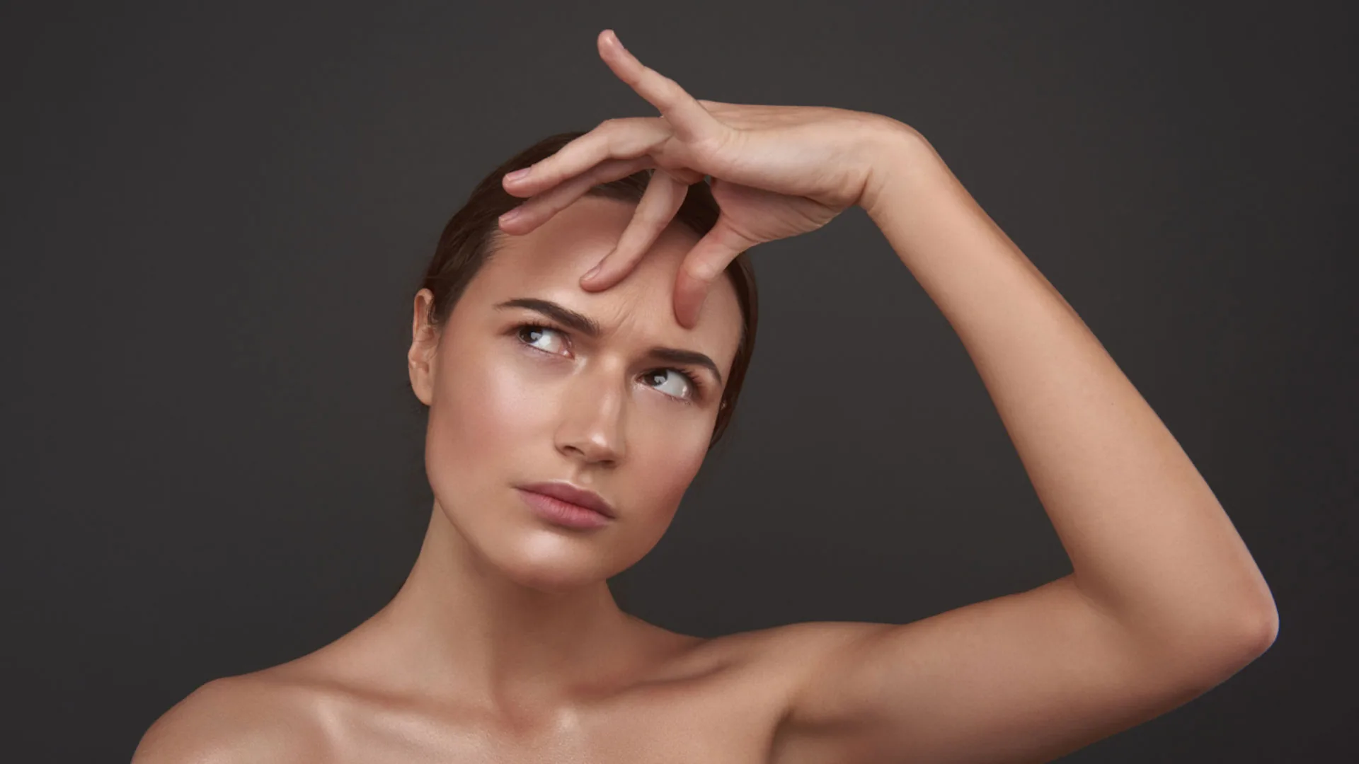 Woman with her hand on her forehead, glancing upward with a furrowed brow
