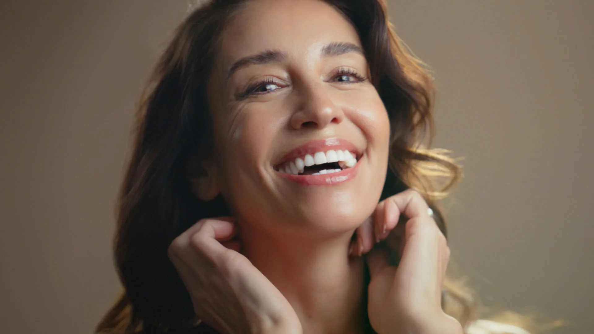 Laughing woman with wavy brown hair touching her neck