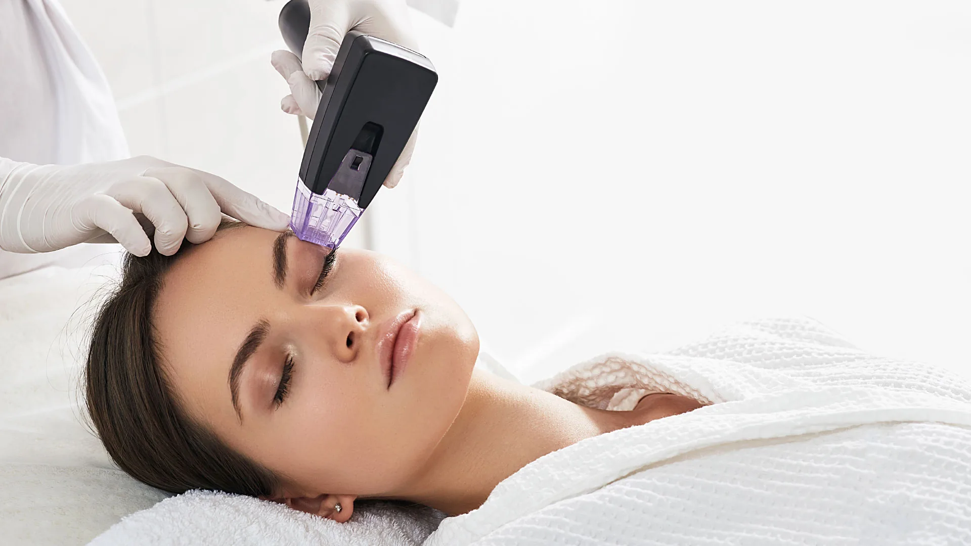 Gloved provider treating a woman's face with a microneedling handpiece as she lies back