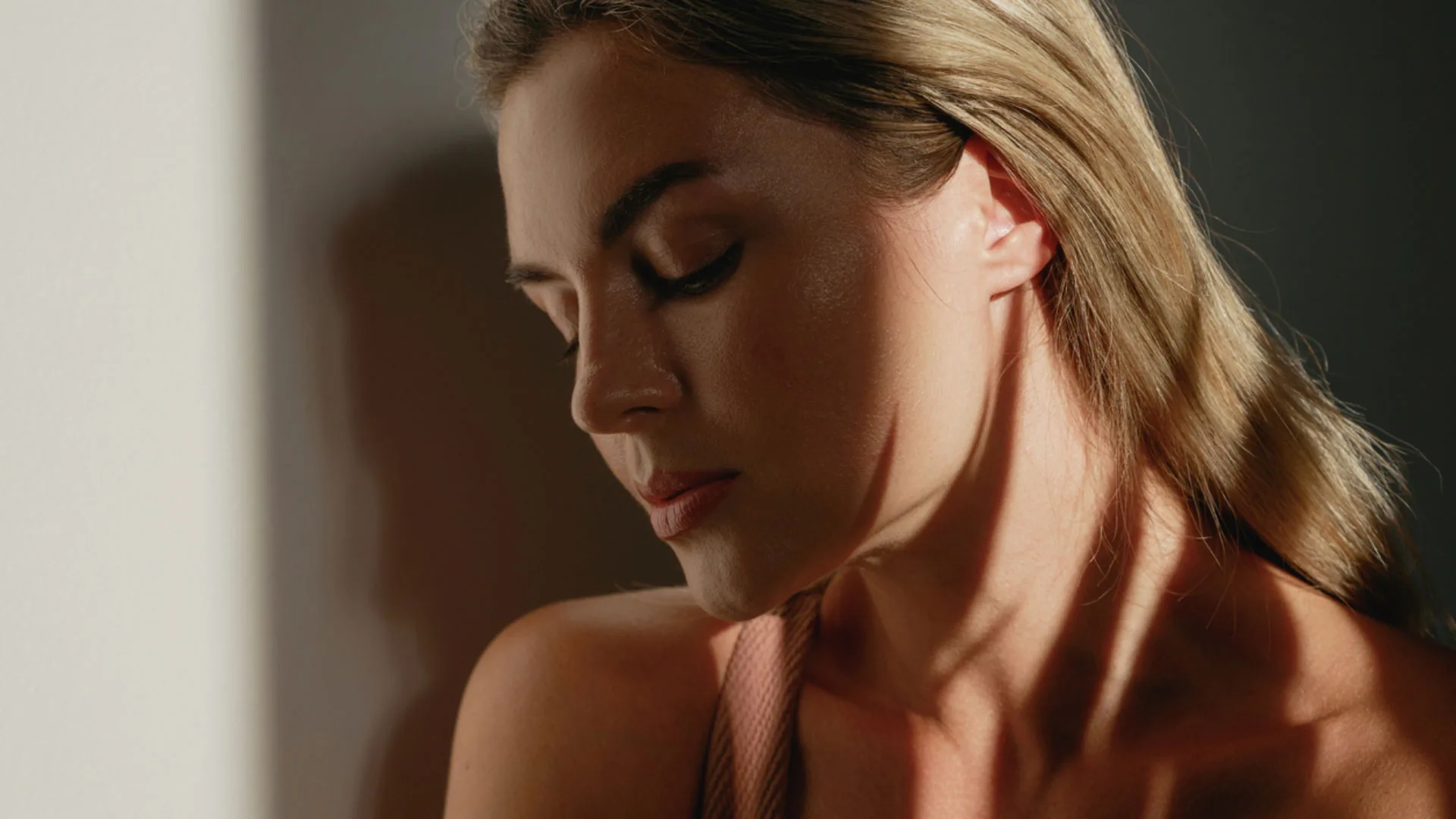 Woman with blonde hair looking down, side light falling across her neck