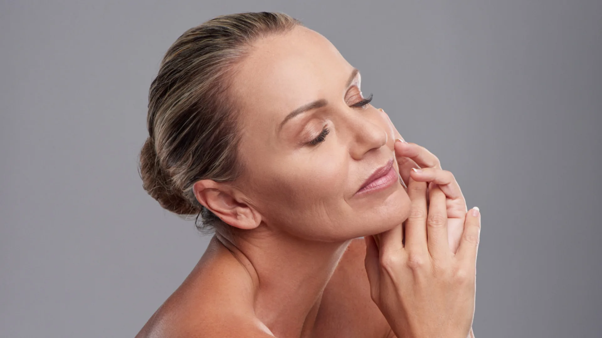 Mature woman with her hair in a bun, eyes closed, hands framing her jaw