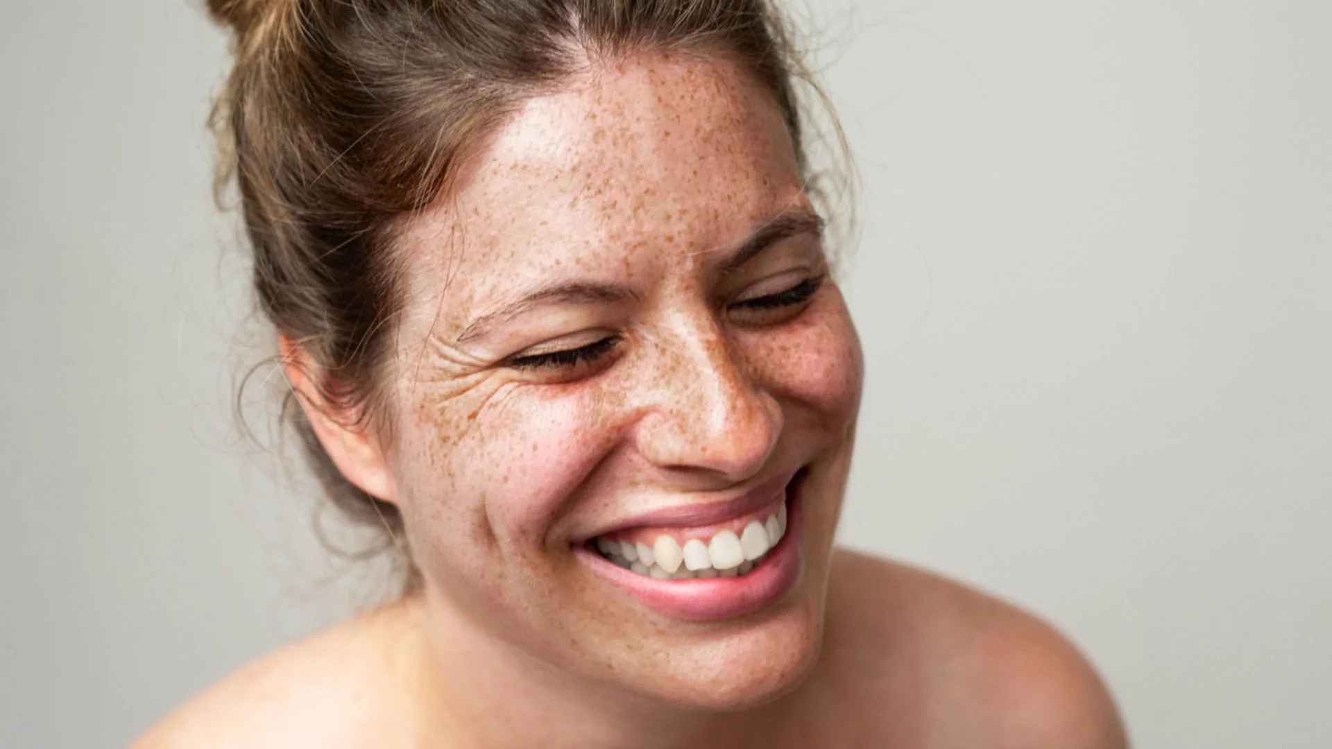 Laughing woman with freckles and her hair pulled back, smile lines visible