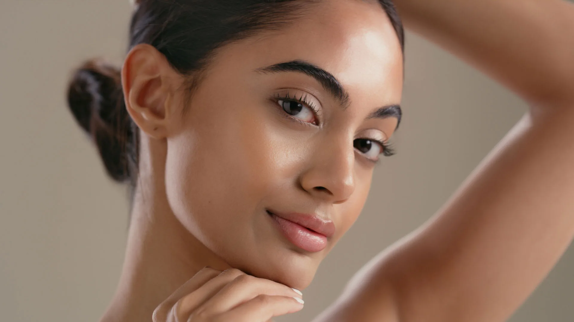 Woman with her hair in a bun resting her chin on her hand, arm raised behind her head