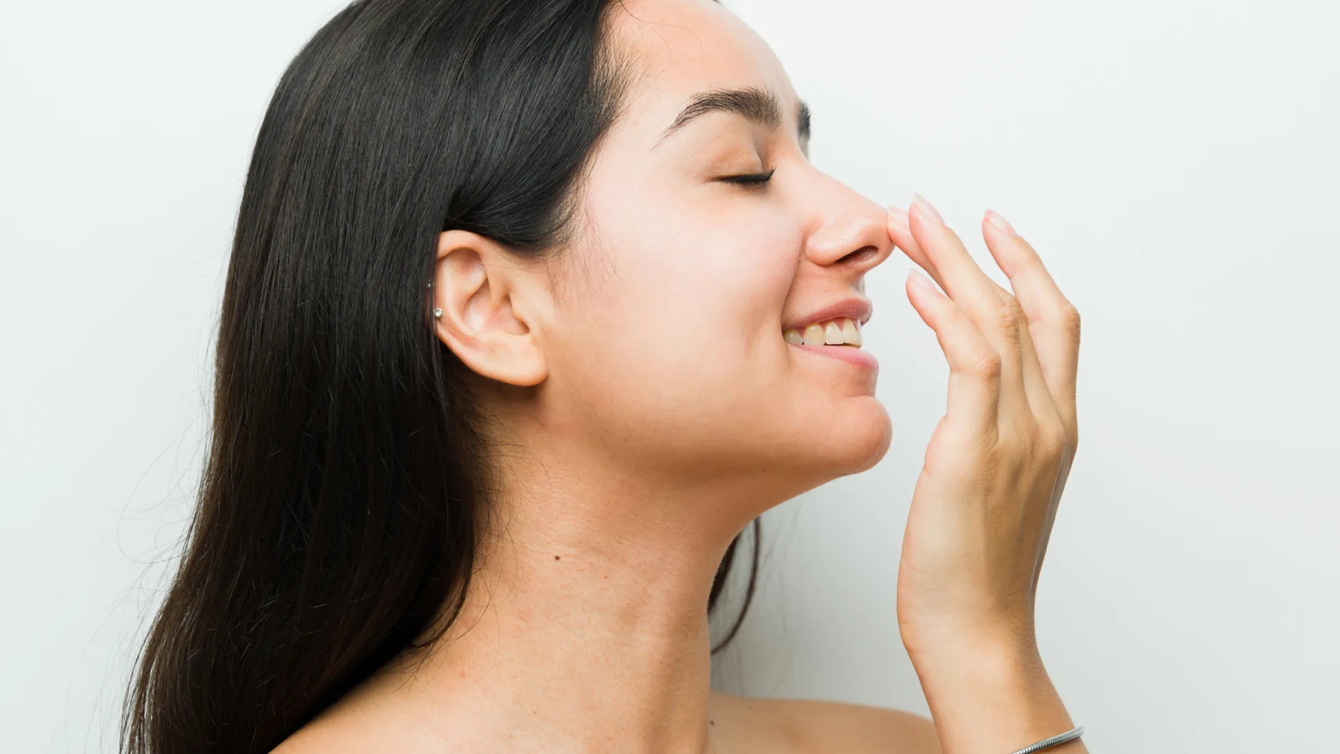 Smiling woman in profile gently touching the tip of her nose