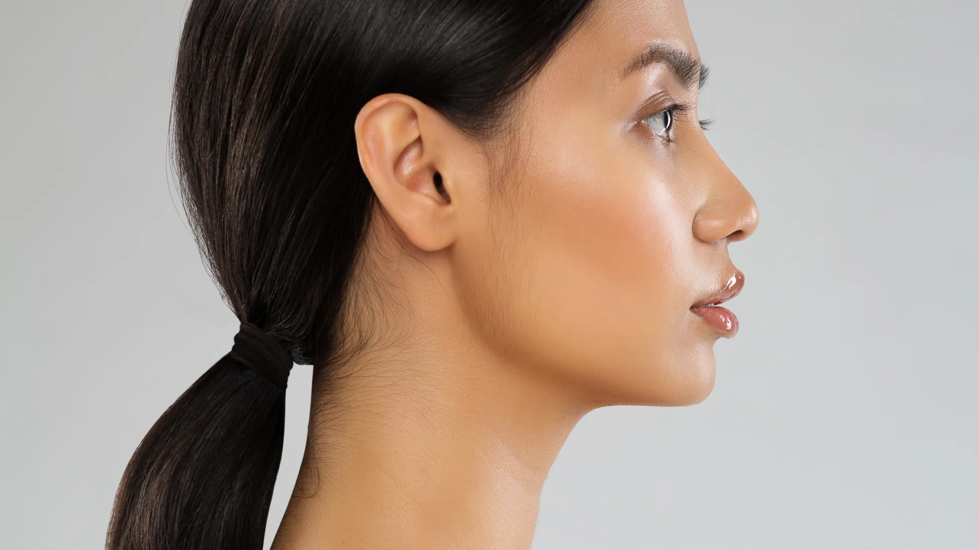 Side profile of a woman with her hair in a low ponytail, highlighting the nose and chin