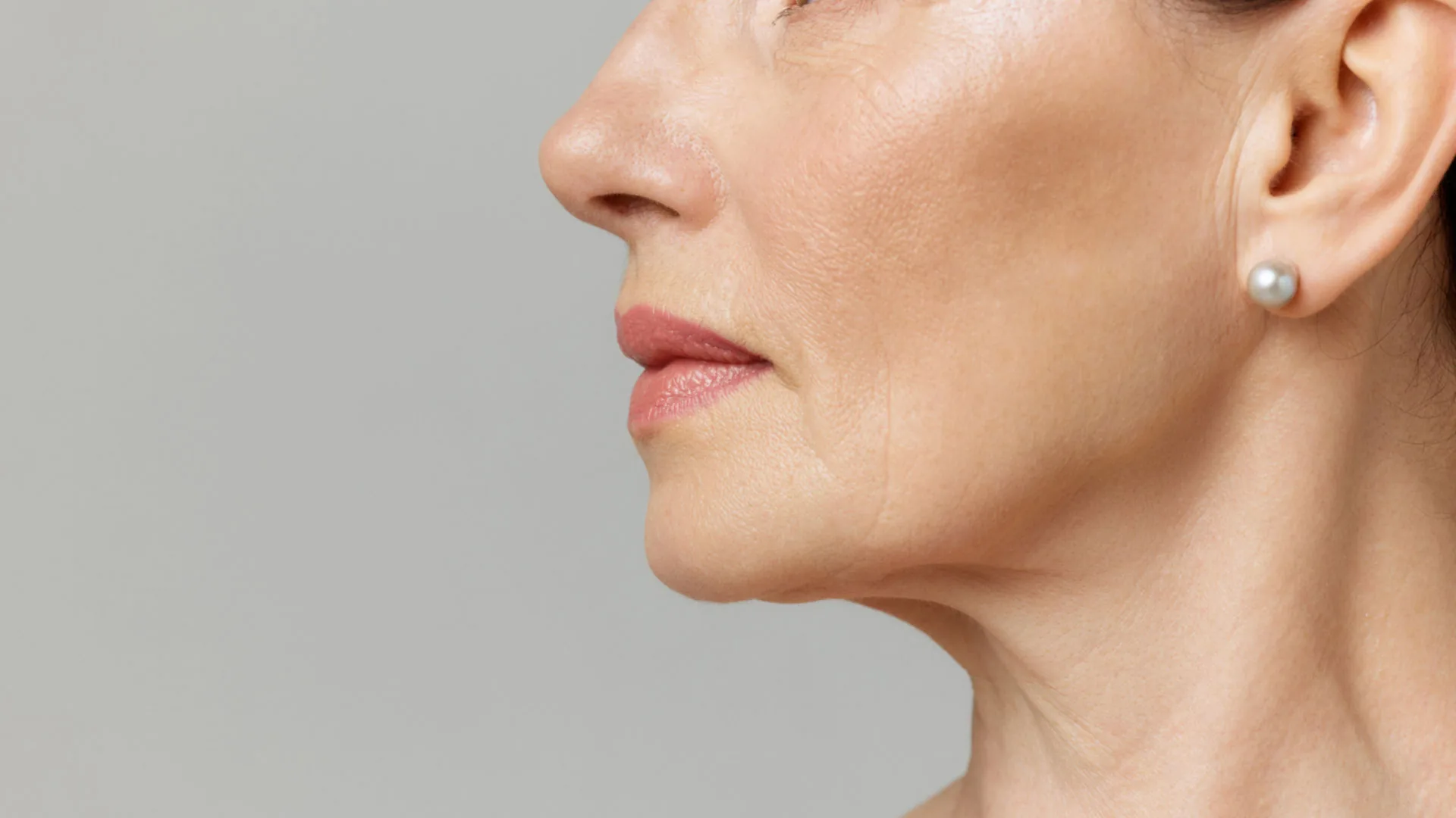 Mature woman's lower face and neck in profile, wearing a pearl earring