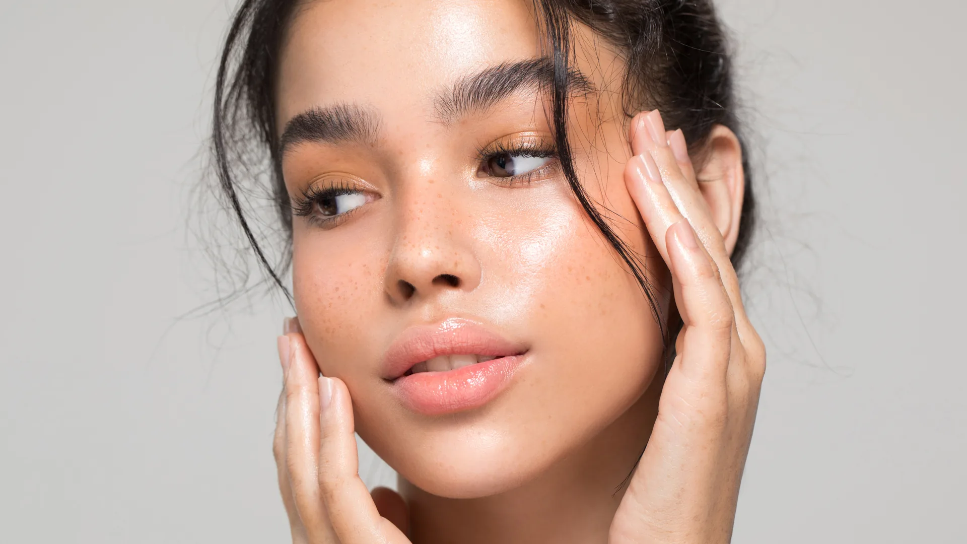 Young woman with freckles framing her face with both hands