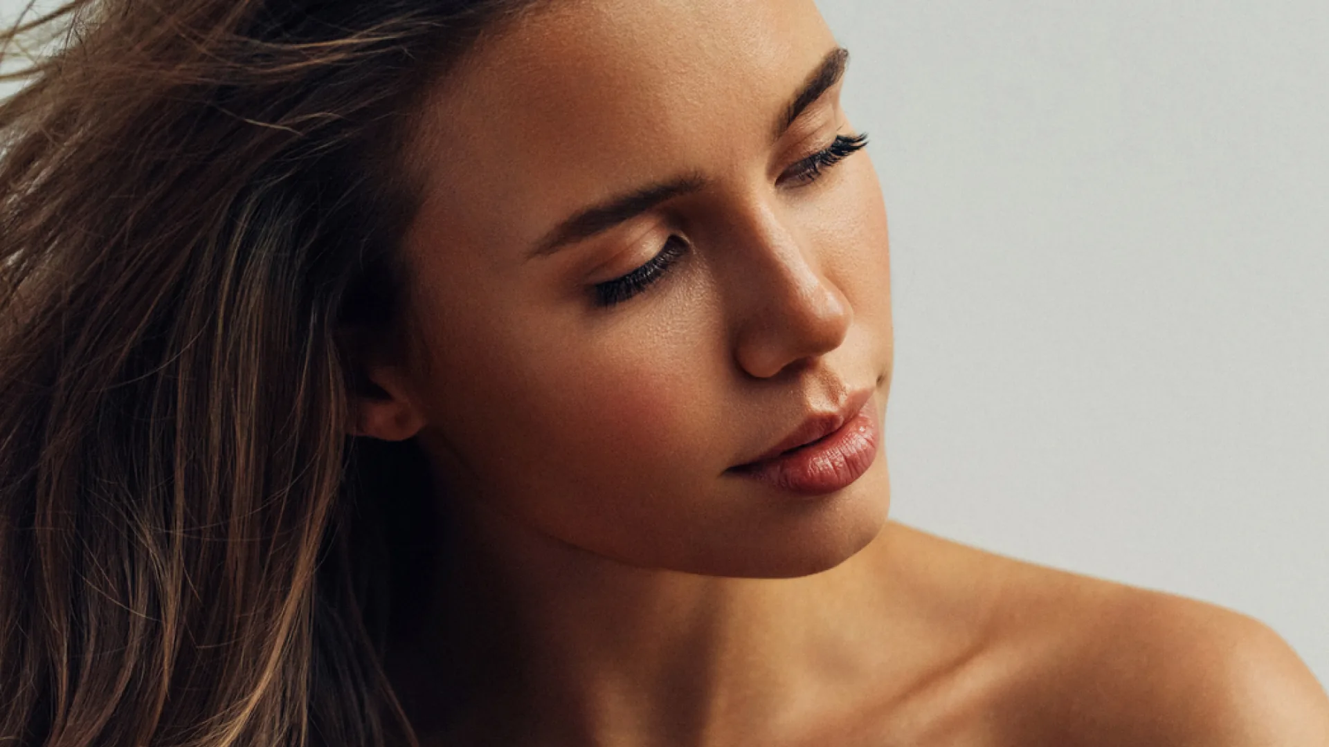 Woman with flowing brown hair looking down, showing her nose and cheek in three-quarter view