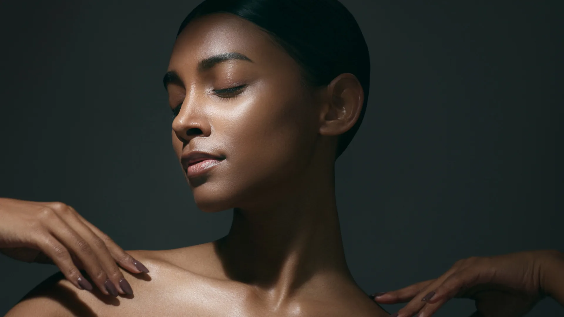 Woman with her hair pulled back and eyes closed, hands resting on her shoulders