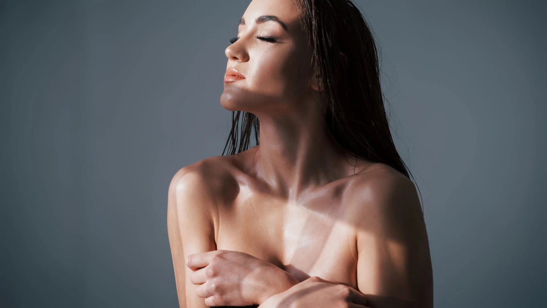 Woman with wet hair and eyes closed in soft side light, arms folded across her chest