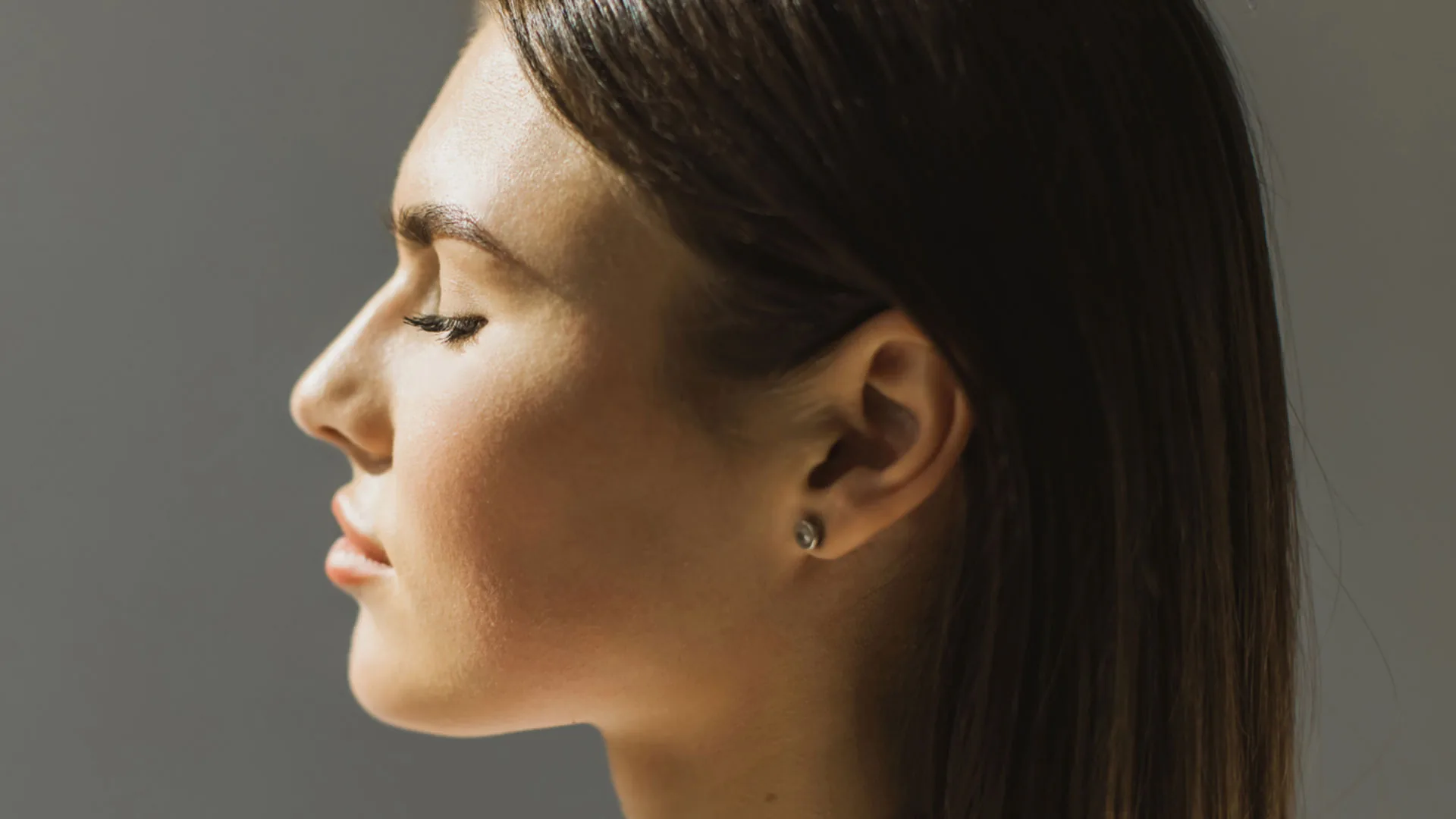 Woman with long hair tucked behind her ear, in profile with eyes closed