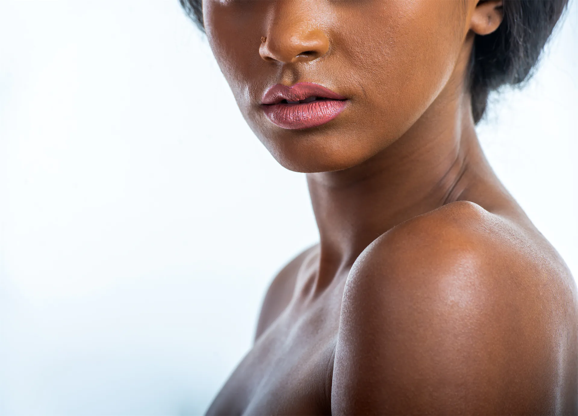 Close-up of a woman's lips, neck, and bare shoulder against a pale background