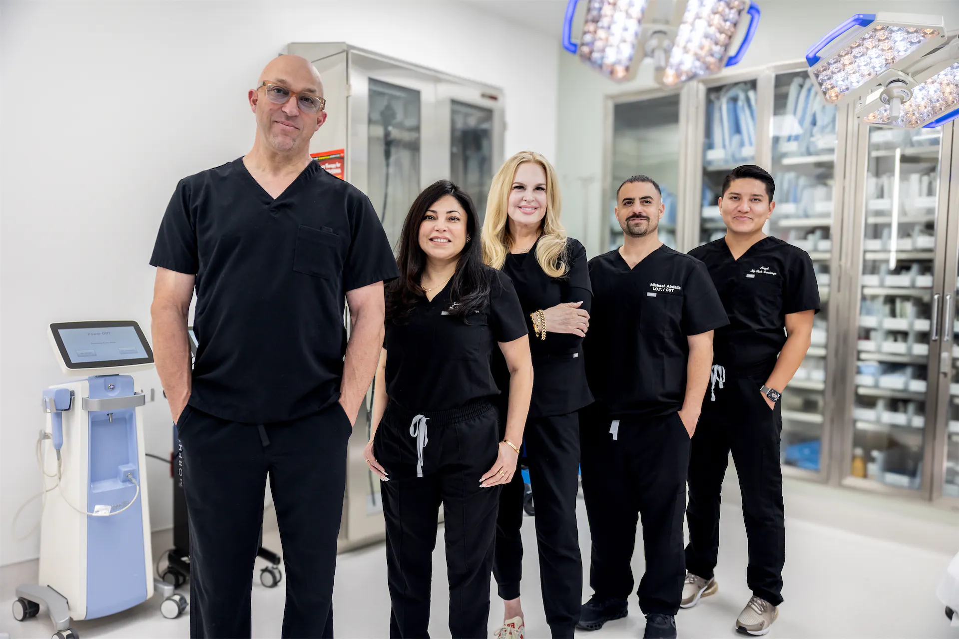 Five GVMD team members in black scrubs posed together in the operating room under surgical lights