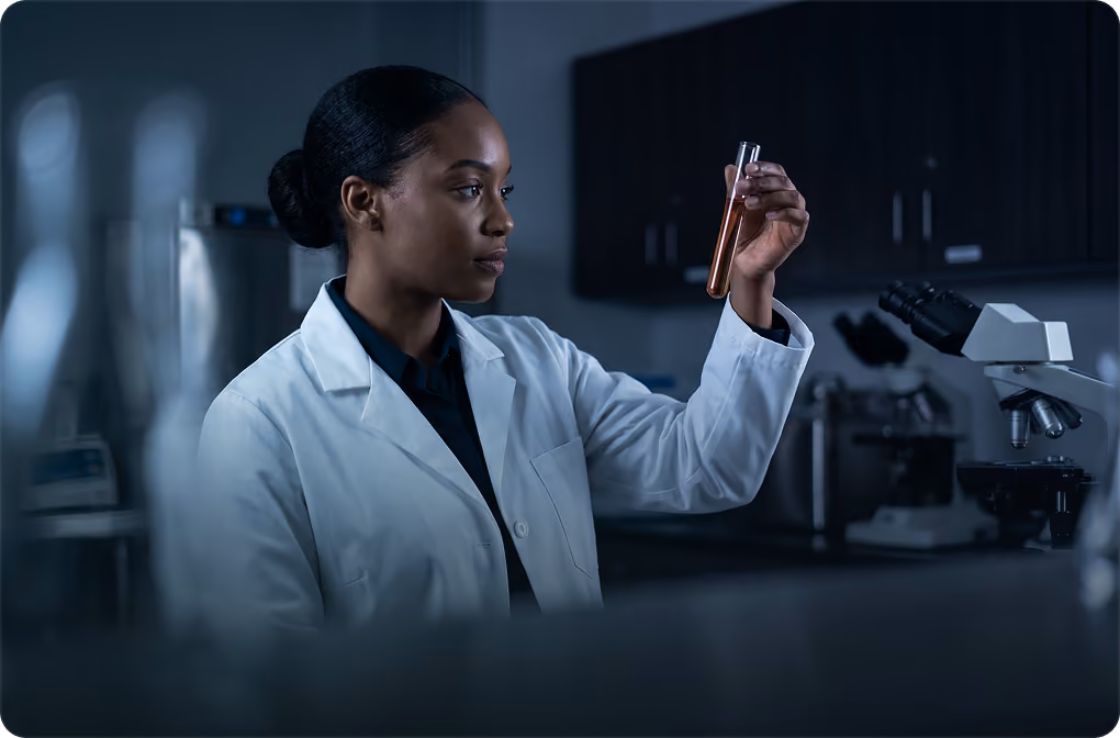 Scientist in a white lab coat holding and examining a test tube in a laboratory.