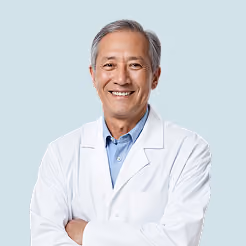 Smiling male doctor with gray hair wearing a white lab coat and blue shirt against a light background.