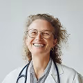 Smiling female doctor wearing glasses and a white coat with a stethoscope around her neck.