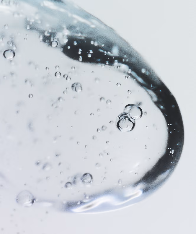 Close-up of small clear bubbles suspended in a transparent liquid against a light background.