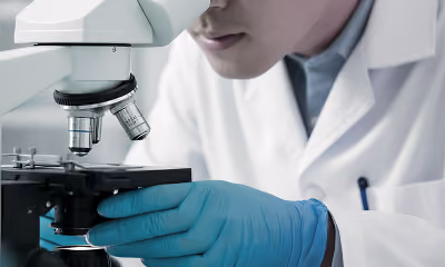 Scientist wearing blue gloves looking into a microscope in a lab setting.