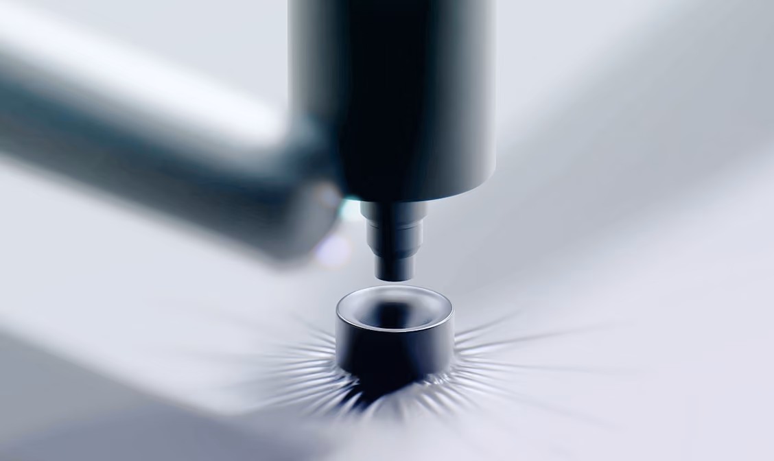 Close-up of industrial machine nozzle above a metal cylinder with light patterns around it.