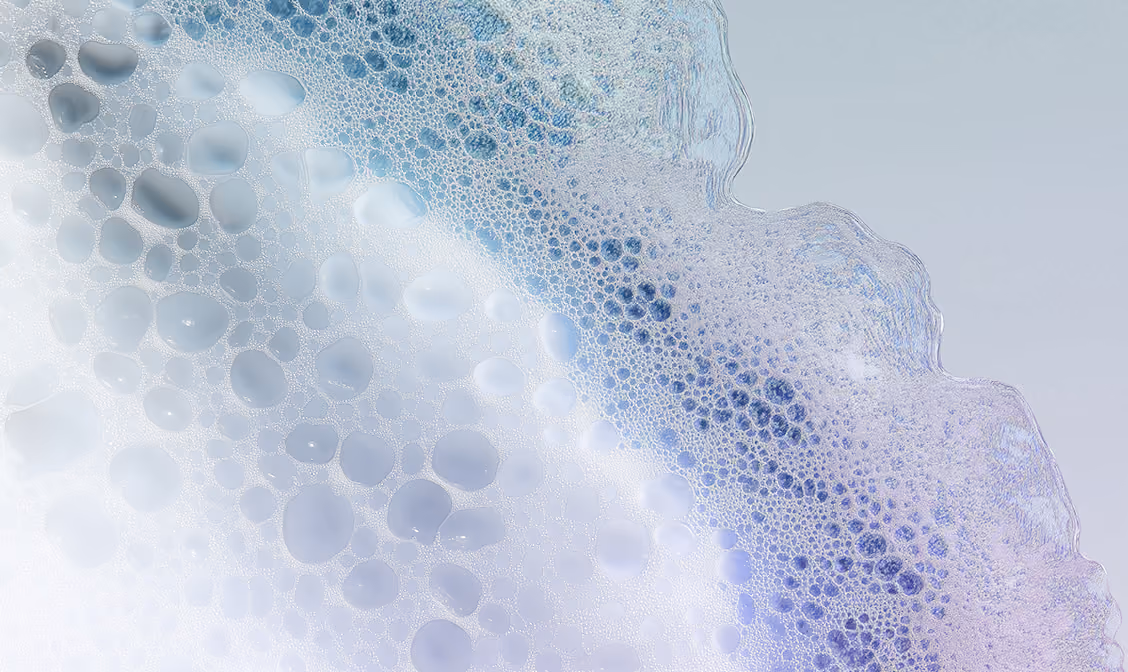 Close-up of soap bubbles foam with blue and purple hues on a light background.