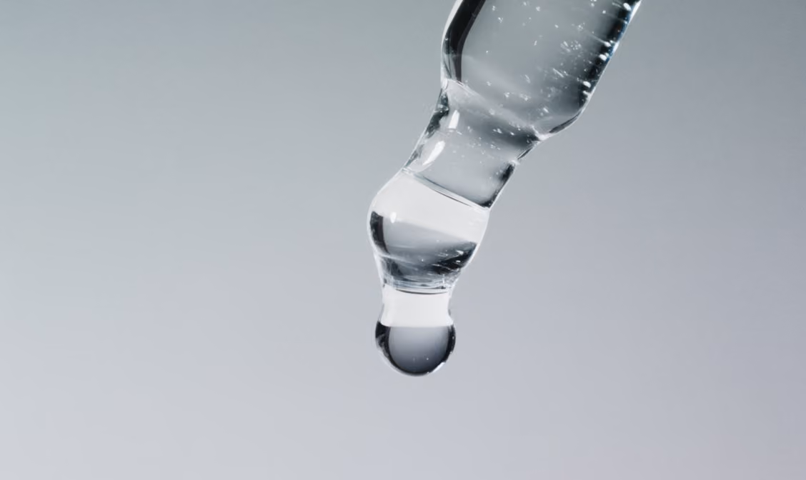 Close-up of a clear dropper with a droplet of liquid at its tip against a neutral background.