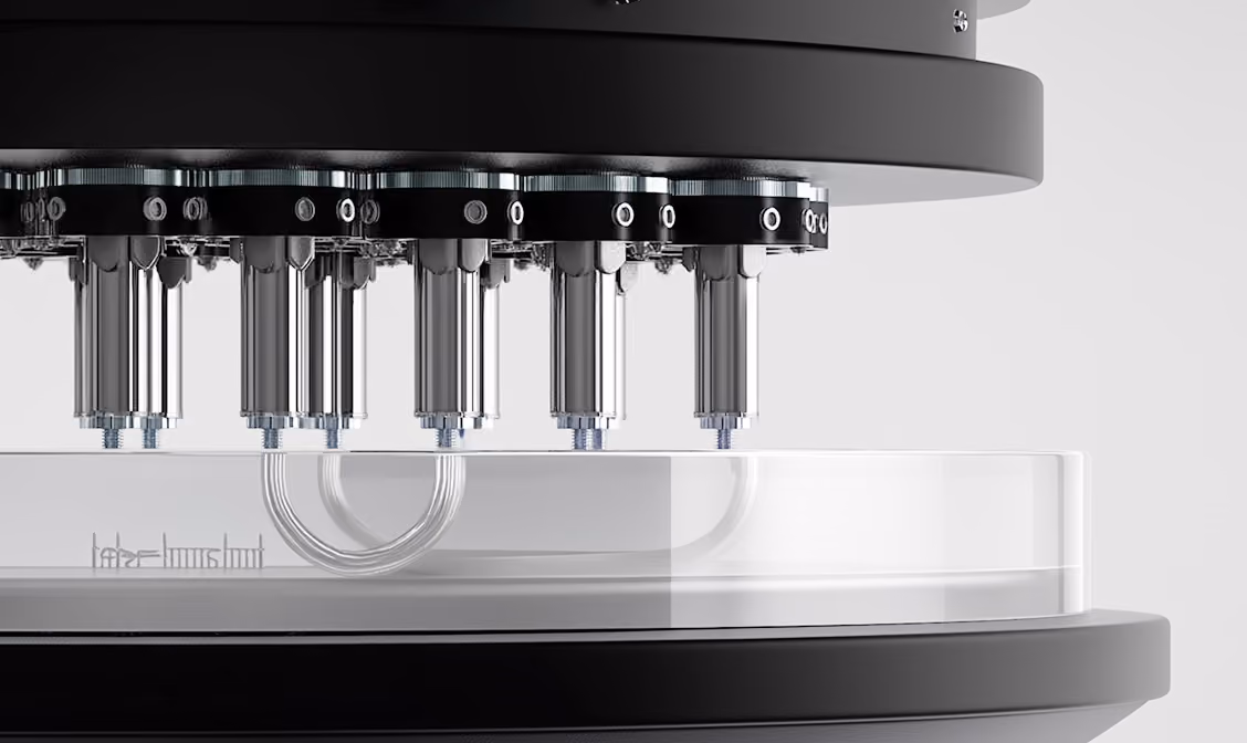 Close-up of a high-tech laboratory device with multiple metallic nozzles above a clear circular platform.