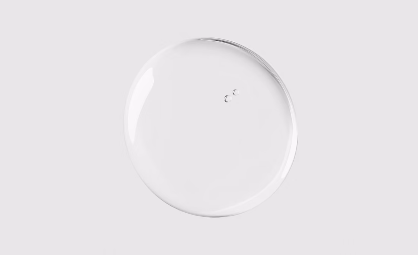 Clear round liquid drop with two small bubbles on a light gray background.