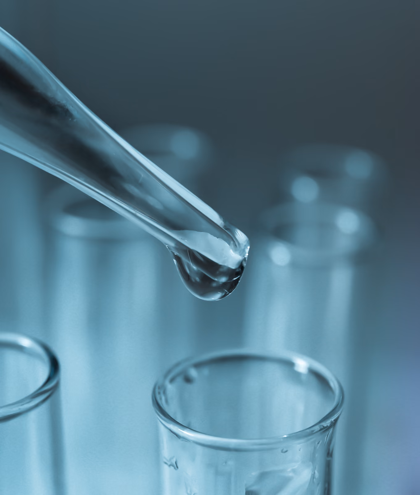Close-up of a dropper releasing liquid into a test tube among other glass test tubes in a lab setting.
