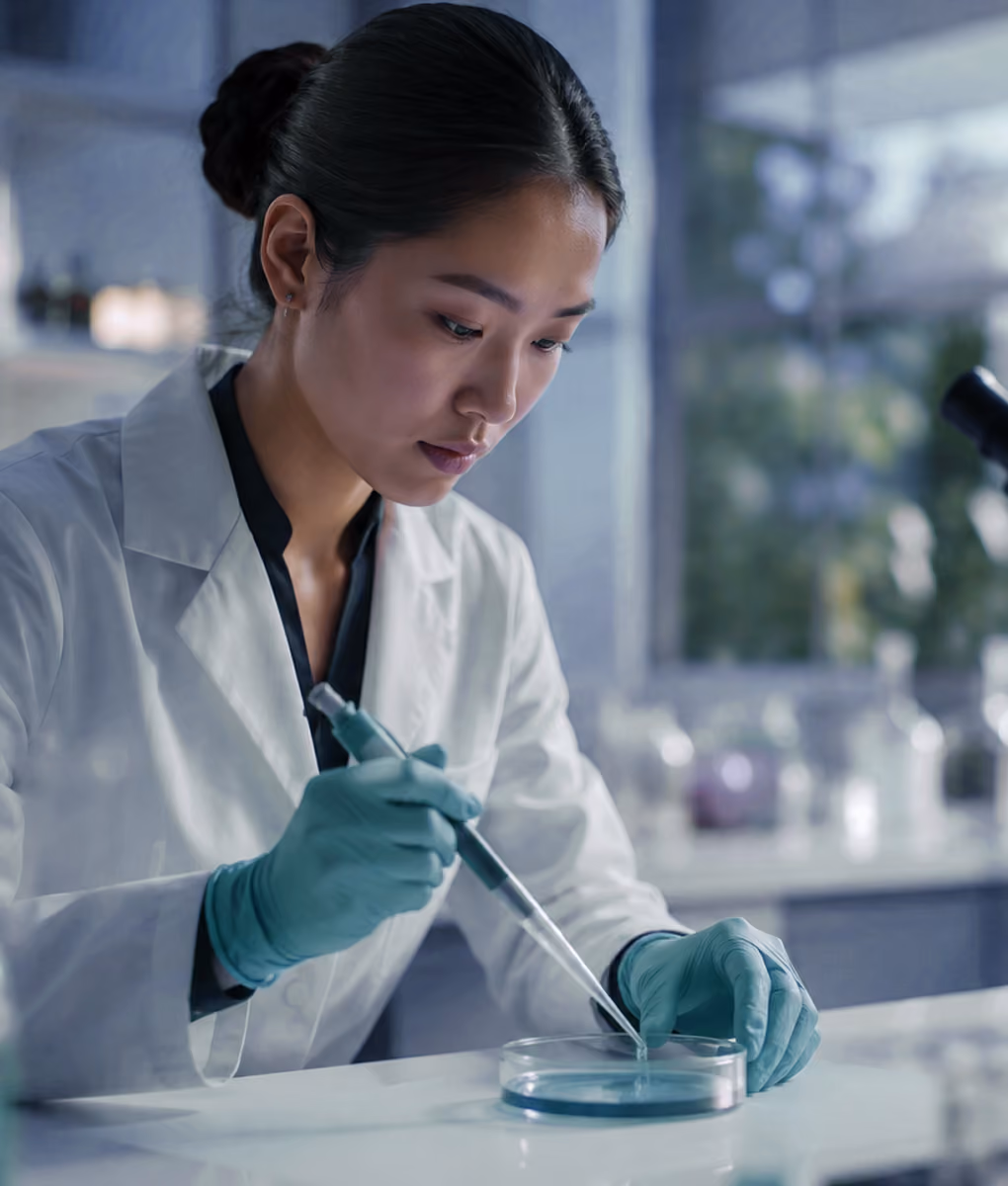 Female scientist wearing gloves and a lab coat using a pipette with a petri dish in a lab.