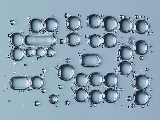 Close-up of transparent bubbles of varying sizes floating on a smooth light blue surface.