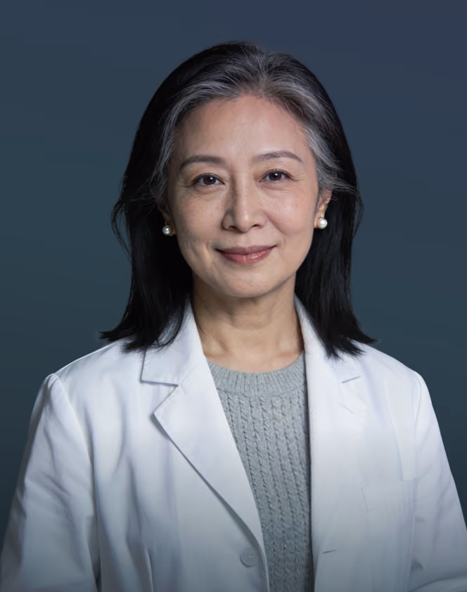 Portrait of a middle-aged Asian woman doctor wearing a white coat and pearl earrings, smiling softly.