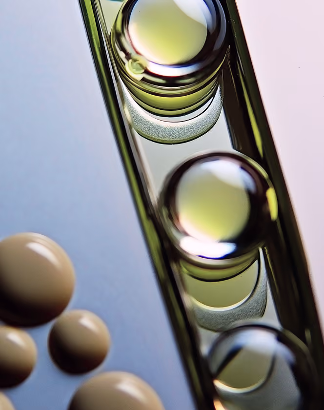 Close-up of three reflective, translucent bubbles aligned vertically and four beige round objects on a blue surface.