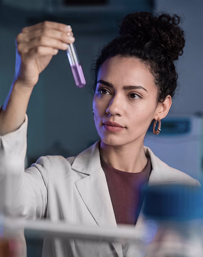 Woman scientist in lab coat examining a test tube with purple liquid in a laboratory.
